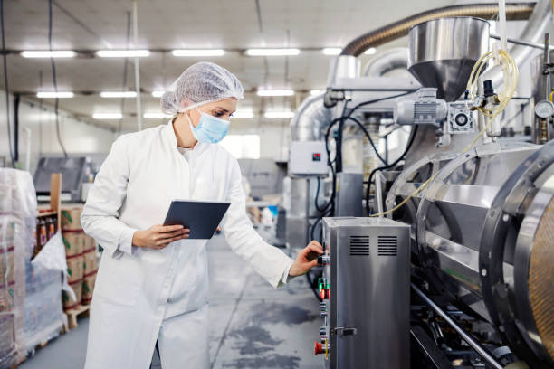 A female milk plant operator holding tablet and adjusting milk processing machine during corona virus.